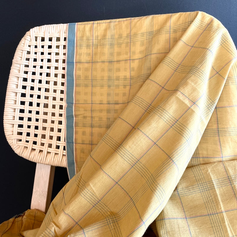 Beige checkered khadi fabric draped over a wicker chair against a dark background