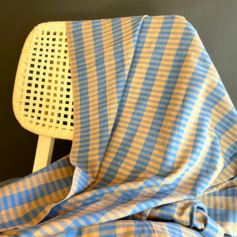 Blue and yellow checkered Khadi fabric draped over a wicker chair against a dark background