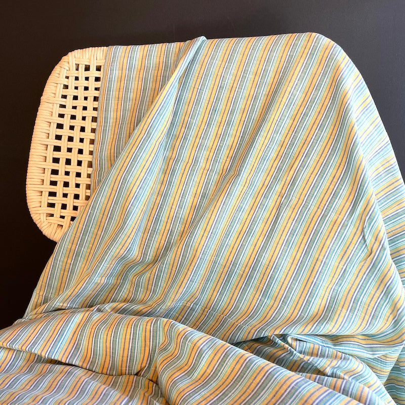 Striped Khadi fabric draped over a wicker chair against a dark background