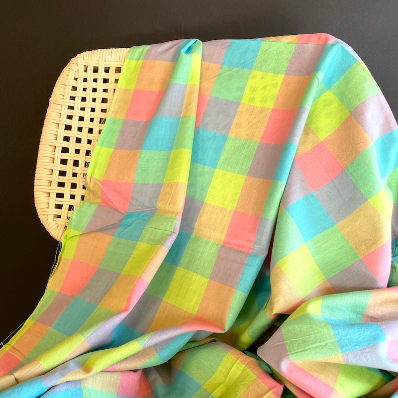 Colorful checkered Khadi fabric draped over a wicker chair against a dark background