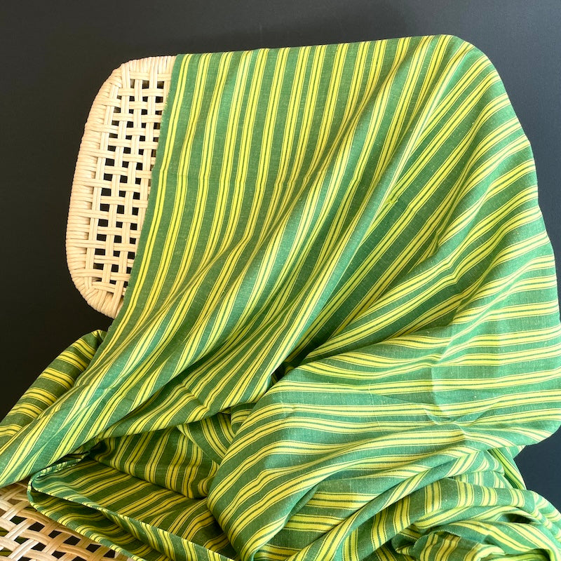 Green and yellow striped Khadi fabric draped over a wicker chair against a dark background