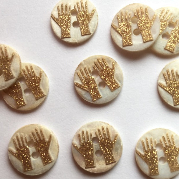 Buttons with gold glittery hand designs on a white background