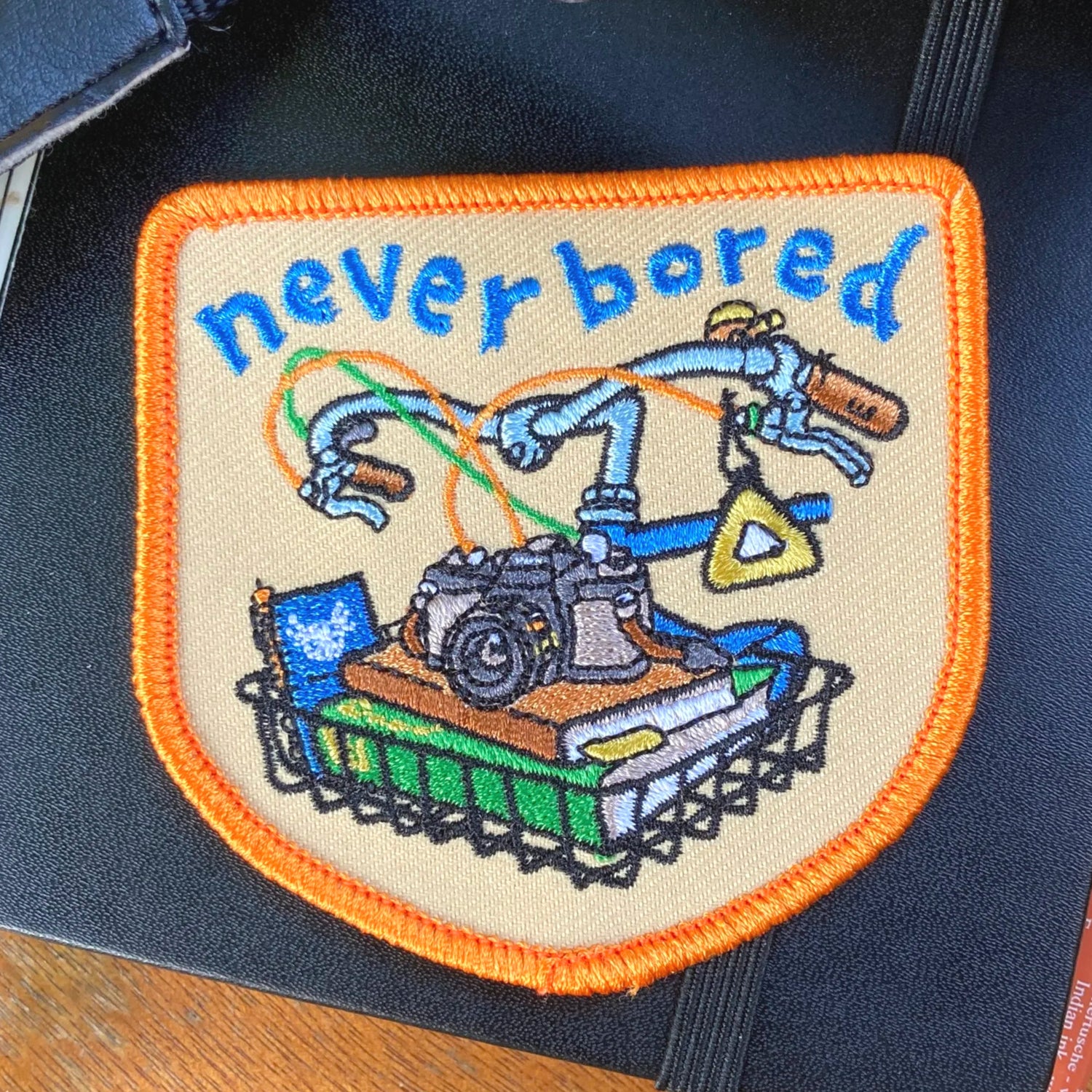 Embroidered patch with robot and 'never bored' text on a dark background