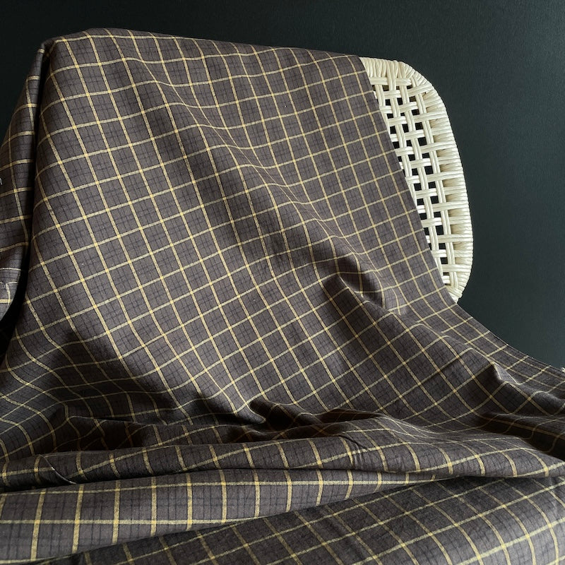 Gray checkered fabric draped over a wicker chair against a dark background