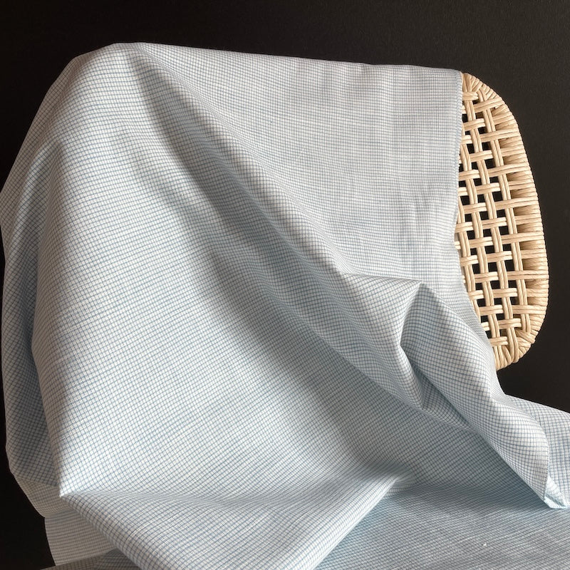 White fabric with small blue grid patter draped over a wicker chair on a black background