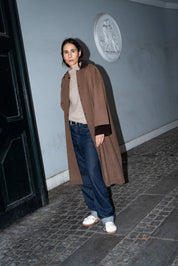 Person wearing a long brown coat standing on a cobblestone street.