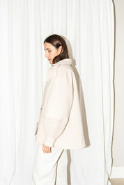 Woman wearing a light-colored coat against a white curtain background