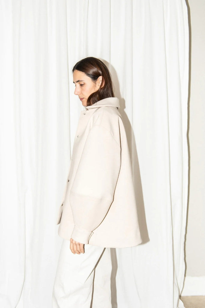 Woman wearing a light-colored coat against a white curtain background