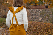 Person wearing mustard yellow overalls with ruffled straps in an outdoor setting with autumn leaves.