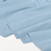 Light blue fabric draped in soft folds over a plain white background.