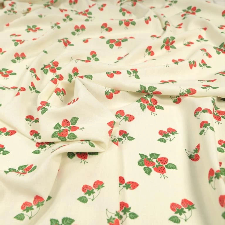 Cream-colored fabric with a repeating pattern of red strawberries and green leaves, draped to show its texture and print.