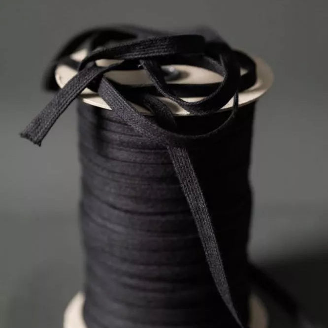 A spool of black ribbon or trim with loose strands draped over the top, photographed against a dark gray studio background.