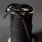 A spool of black ribbon or trim with loose strands draped over the top, photographed against a dark gray studio background.
