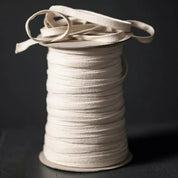 A spool of off-white or cream-colored elastic cord or ribbon, photographed on a dark black background.