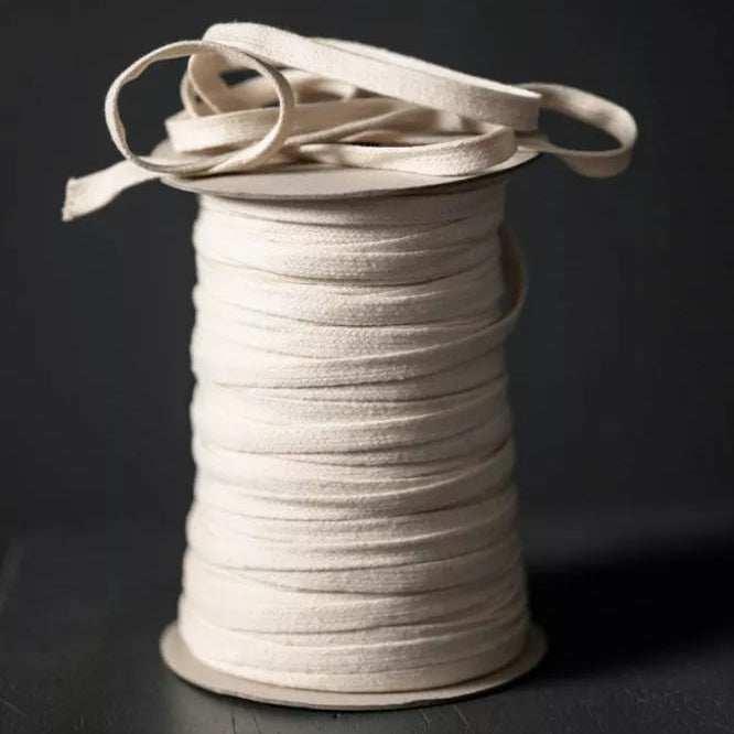 A spool of off-white or cream-colored elastic cord or ribbon, photographed on a dark black background.