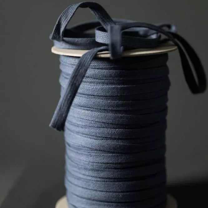 A spool of dark navy blue cord or ribbon with a few loose strands draped over the top, set against a dark gray background.