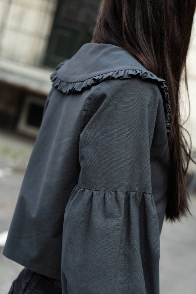 Dark gray jacket with ruffled collar worn by a person, blurred background