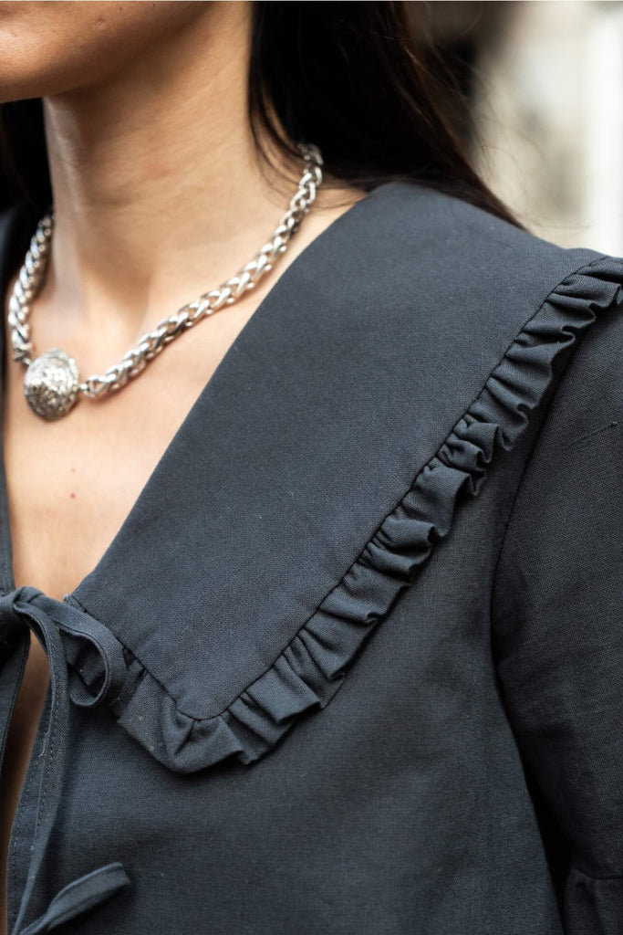 Close-up of a person wearing a dark blue blouse with ruffled collar and a silver necklace.