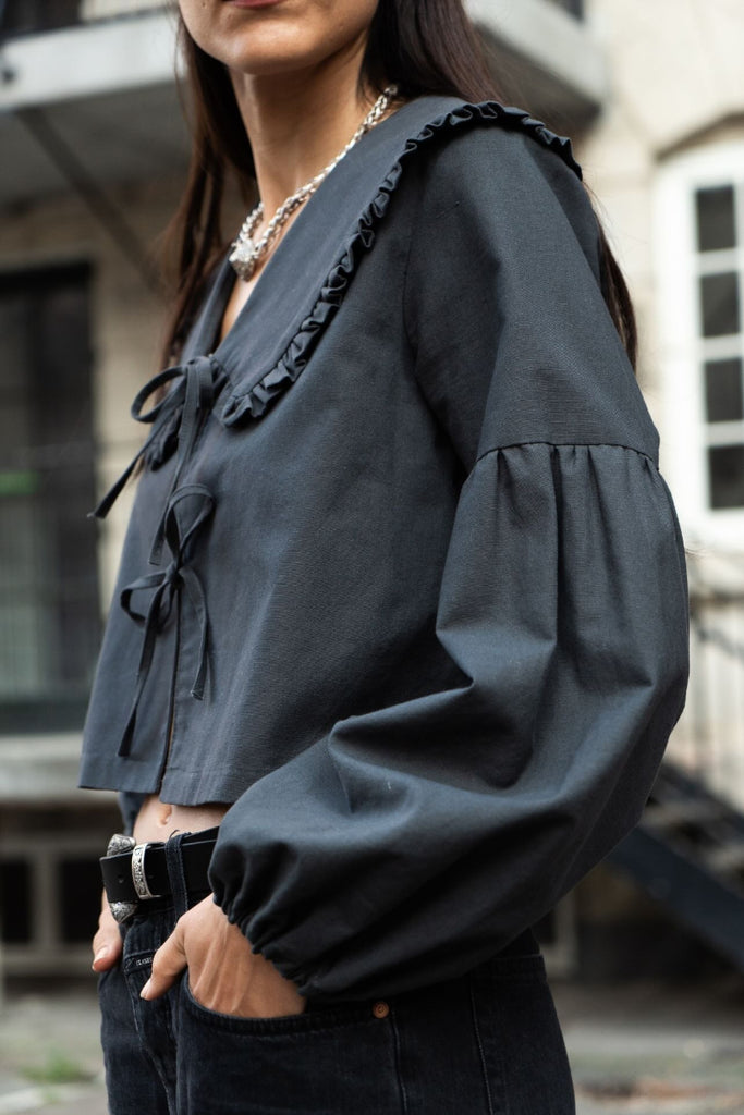 Person wearing a dark blue blouse with ruffled details in an urban setting