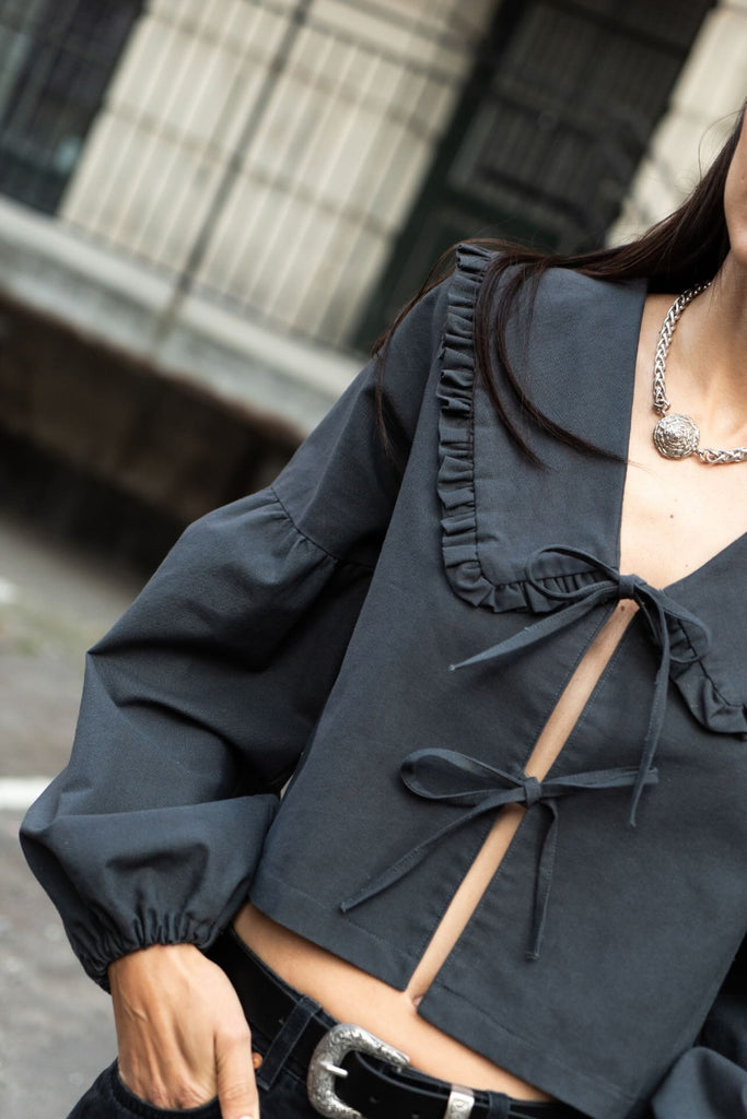 Black blouse with ruffled details and a bow tie worn by a person, blurred background