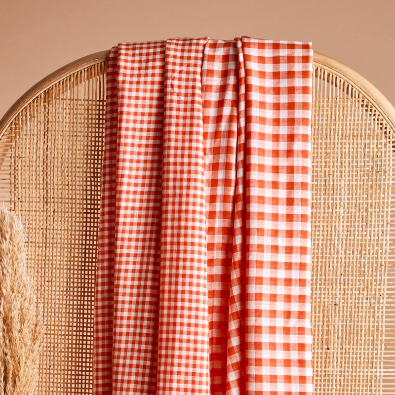 Orange and white checkered fabric draped over a wicker chair on a beige background