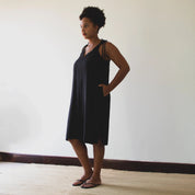 person wearing a black dress standing against a plain wall.
