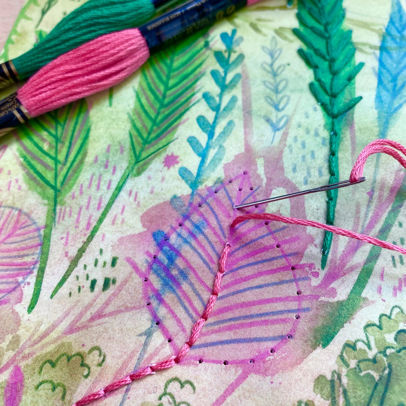 Embroidery hoop with floral pattern and pink thread, surrounded by embroidery tools.