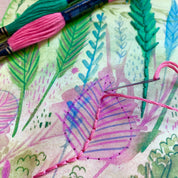 Embroidery hoop with floral pattern and pink thread, surrounded by embroidery tools.