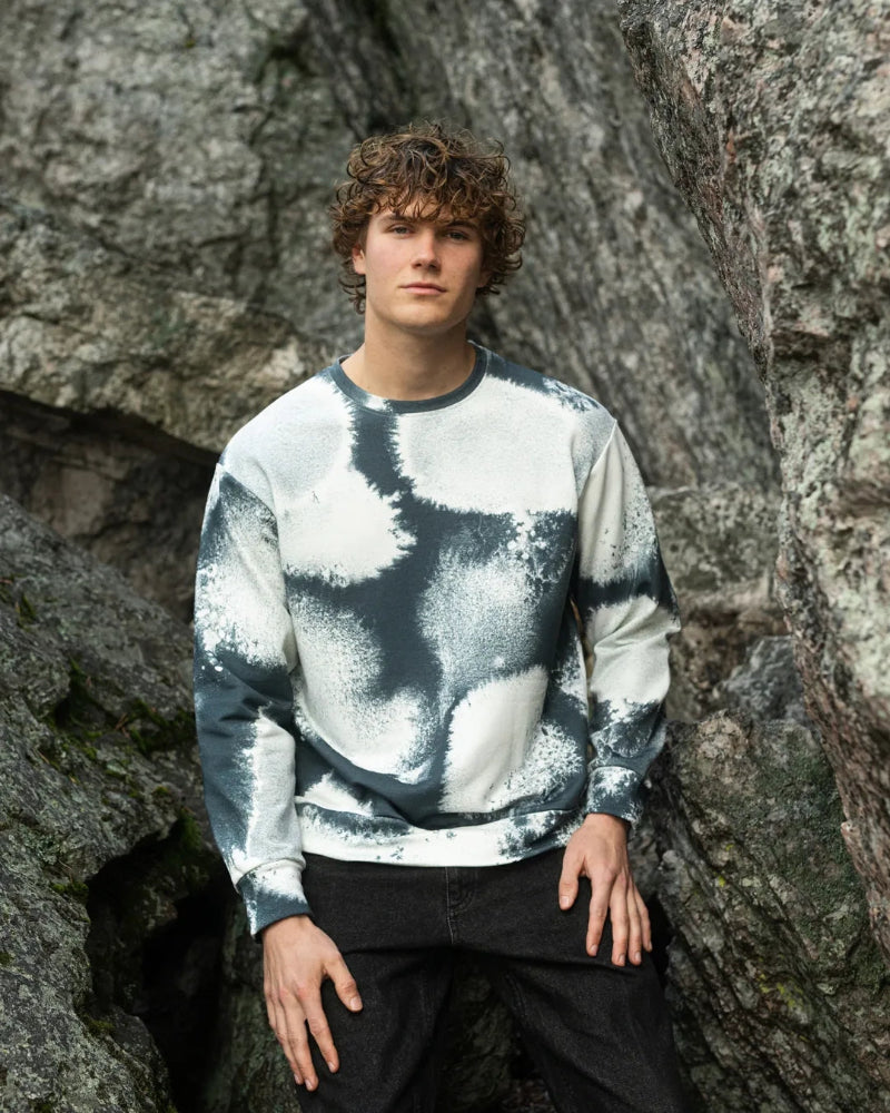Person wearing a tie-dye sweater standing against a rocky background