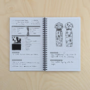 Open notebook on a wooden surface with fashion sketches and notes.