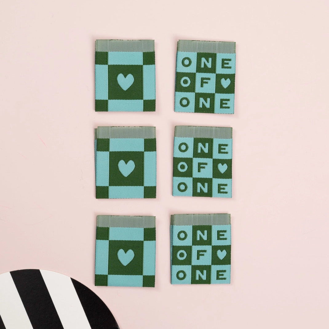 Set of five green and blue checkered labels with heart designs on a pink background.
