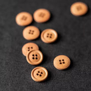 Several small round wooden buttons with four holes, in natural light brown wood, scattered on a dark textured fabric background.