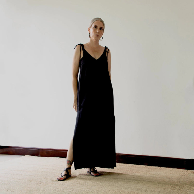 person wearing a black slip dress standing against a plain wall.