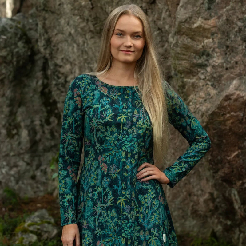 Woman wearing a green floral dress standing in front of a rocky background