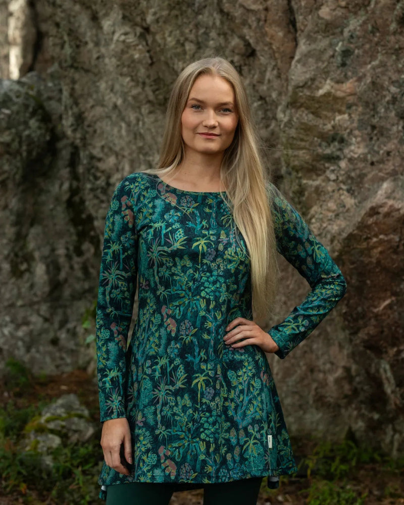 Woman wearing a green floral dress standing in front of a rocky background