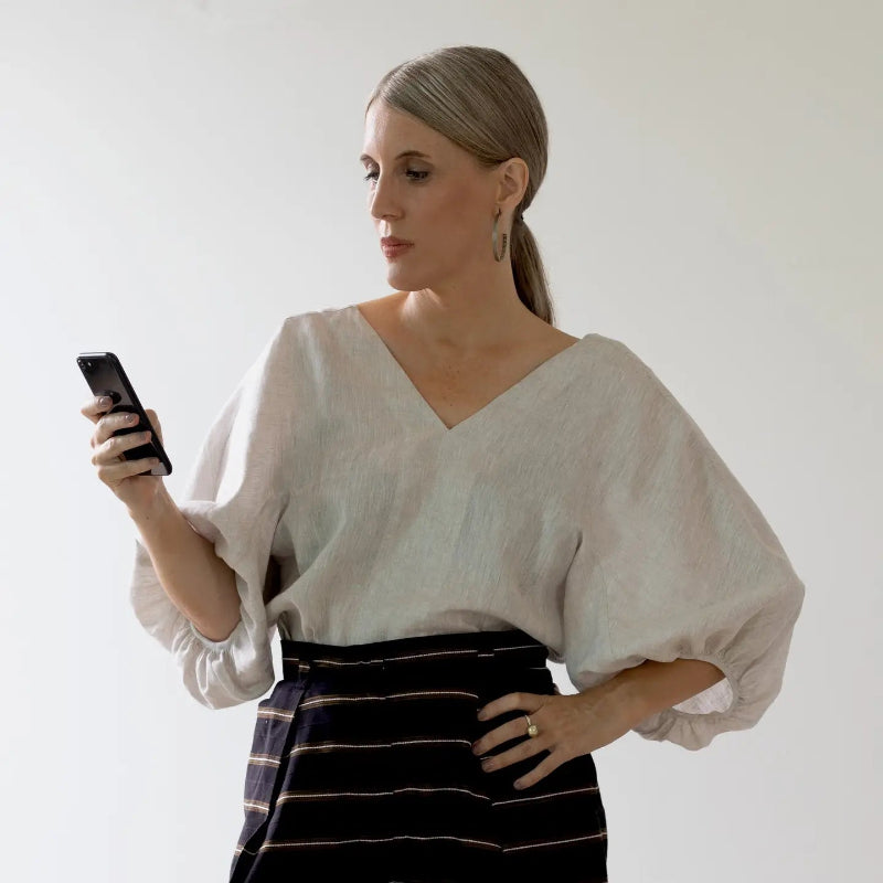 person in a white blouse and striped skirt holding a phone against a plain background