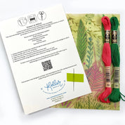 Embroidery kit with red and green thread on a card featuring instructions and branding.