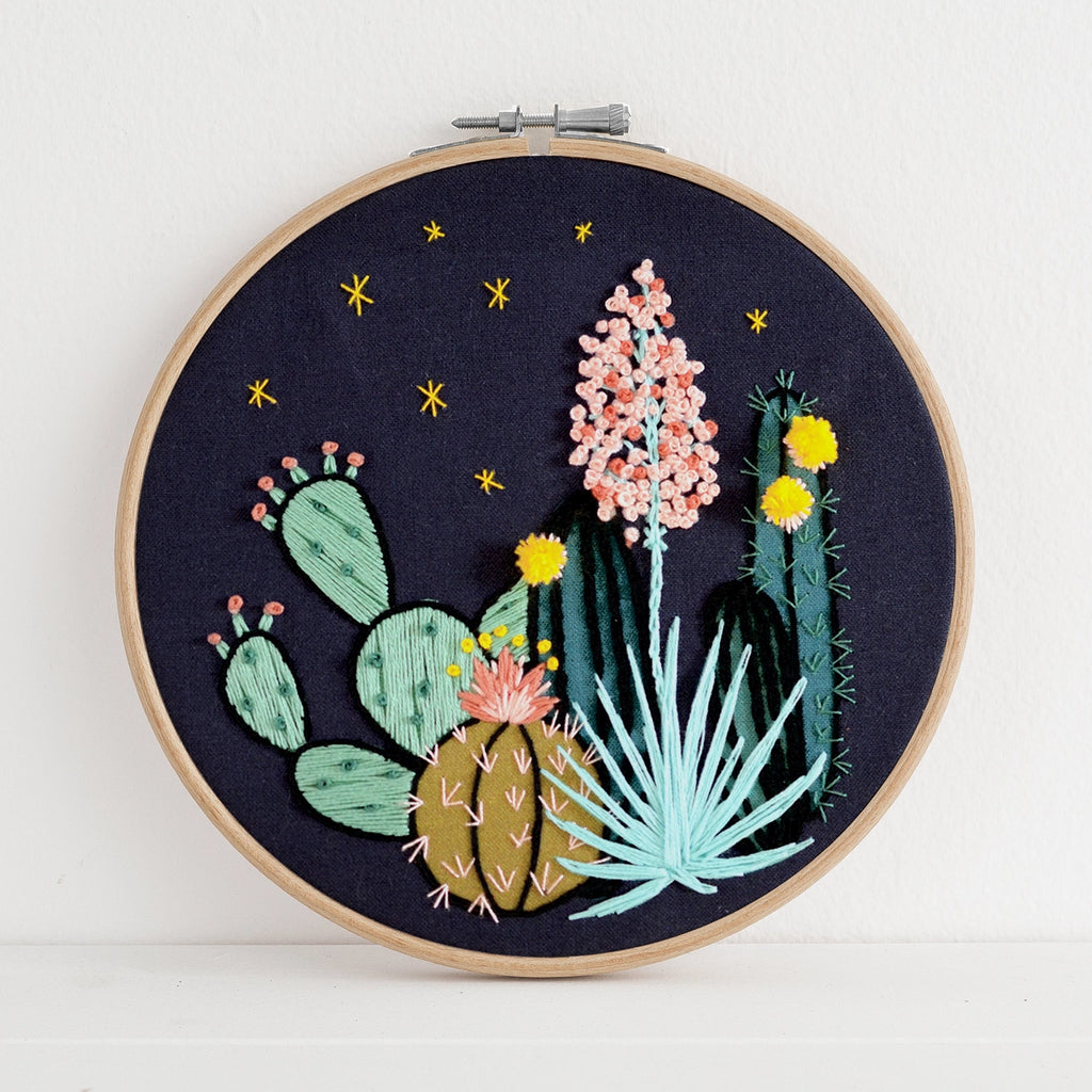 Embroidery hoop with embroidered cacti and flowers on a dark background