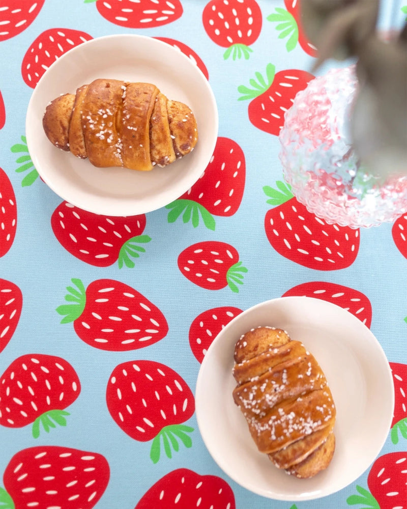 Two croissants on white plates with a strawberry patterned background