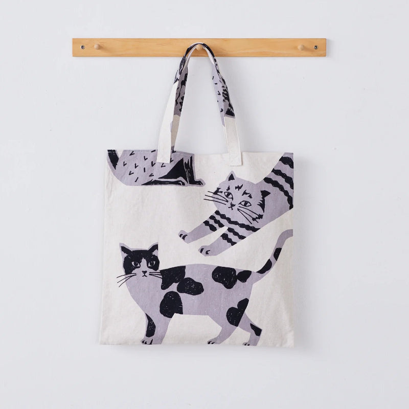 Tote bag with cat design hanging on a wooden rod against a white background