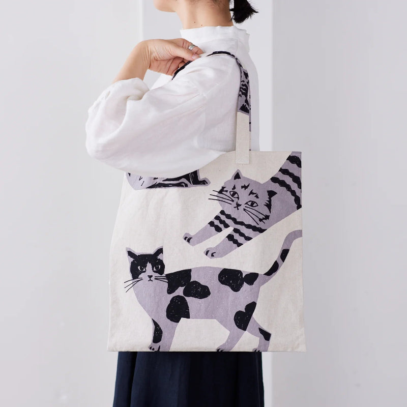 Person holding a tote bag with cat pattern against a plain background