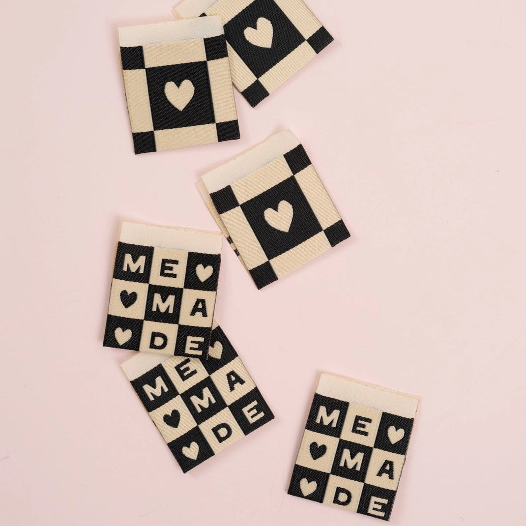 Six labels featuring a checkerboard pattern with hearts and words "me made" on a pink background