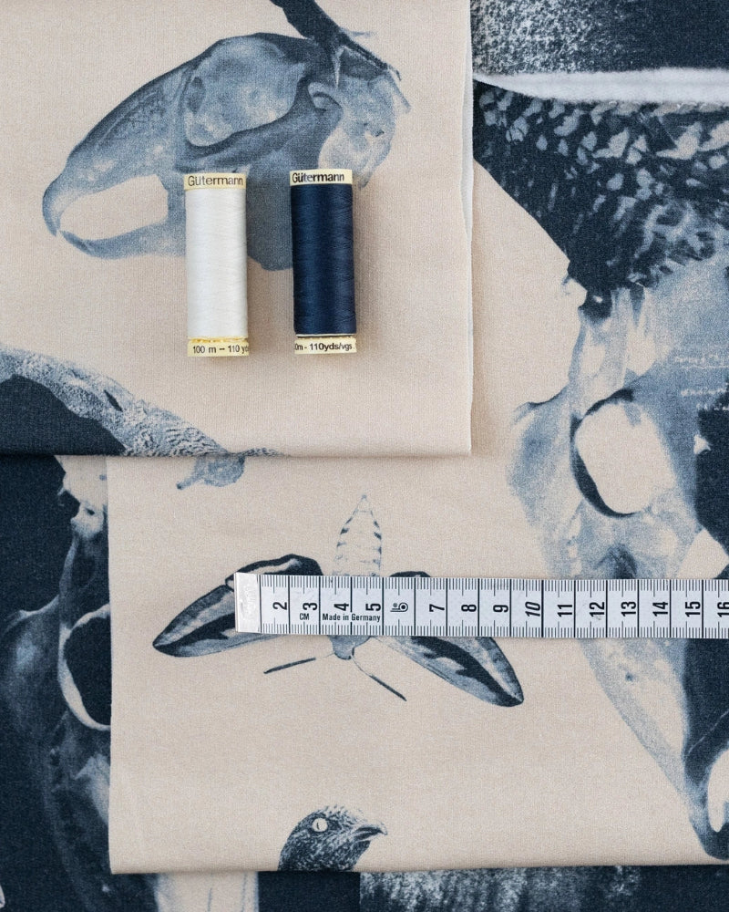 Two spools of thread and a measuring tape on fabric with bird designs.