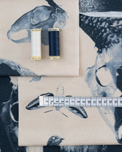 Two spools of thread and a measuring tape on fabric with bird designs.