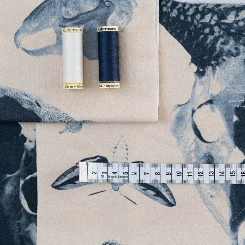 Two spools of thread and a measuring tape on fabric with bird designs.