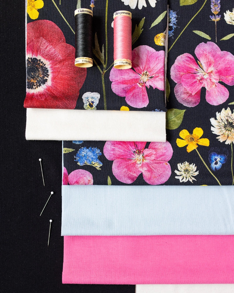 Floral fabric swatches with spools of thread and pins on a black background