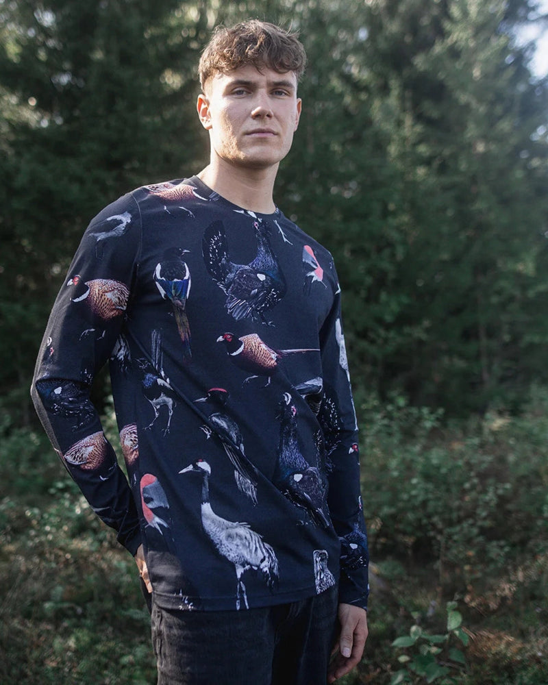 Man wearing a dark long-sleeve shirt with animal patterns standing in a forest.