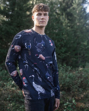 Man wearing a dark long-sleeve shirt with animal patterns standing in a forest.