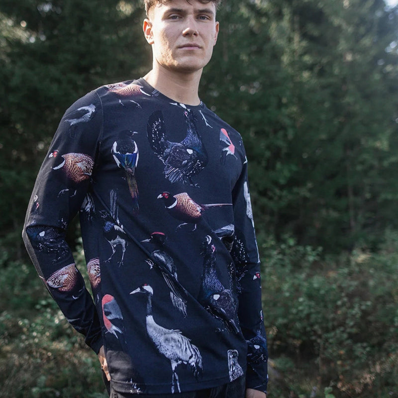 Man wearing a dark long-sleeve shirt with animal patterns standing in a forest.