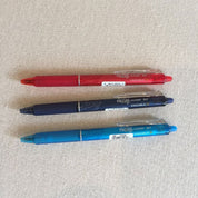 Three gel erasable pens in red, blue, and black colors, displayed on a textured surface.